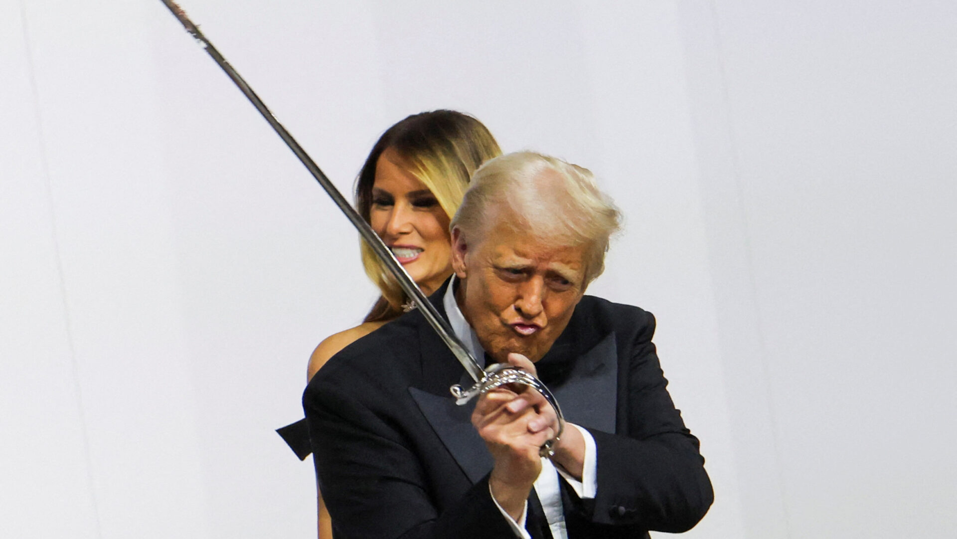 U.S. President Donald Trump gestures while holding a sword, near first lady Melania Trump, as they attend the Commander in Chief Ball in honor of his inauguration in Washington, U.S., January 20, 2025. REUTERS/Daniel Cole